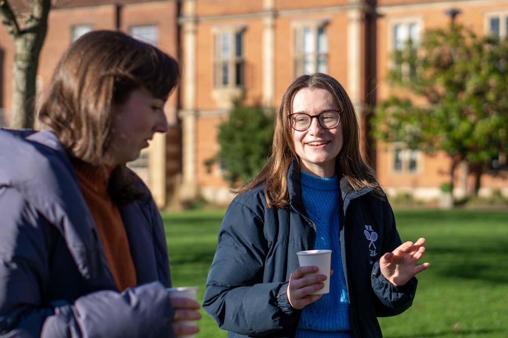 Youth talking to woman in park with coffee.